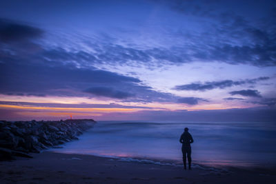 Full length rear view of person standing on shore against sky at sunset