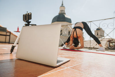 Young sporty fit woman coach doing online lessons through video call on her mobile phone and laptop
