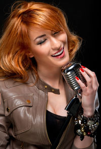 Smiling young woman singing on microphone against black background