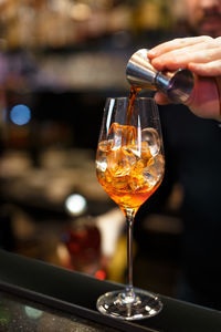 Bartender is preparing an aperol cocktail. hand pours orange liquid into a glass of ice.