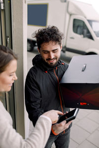 Female customer signing on smart phone while receiving box from delivery man