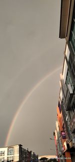 Low angle view of rainbow over buildings against sky