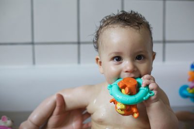 Portrait of cute shirtless baby boy with toy having bath in bathroom