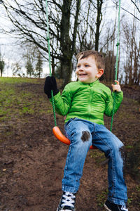 A young boy with muddy jeans plays on a swing in the woods