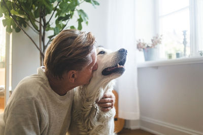 Close-up of retired senior man kissing retriever while sitting at home