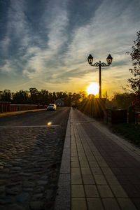 Street lights on road against sky at sunset