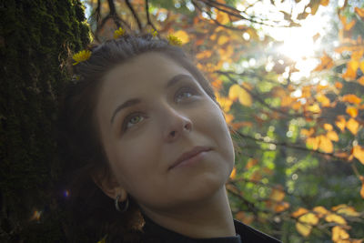 Portrait of young woman looking away against trees