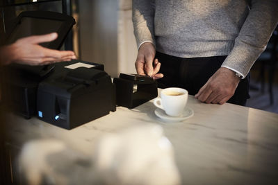 Midsection of male customer paying through credit card at checkout counter in cafe