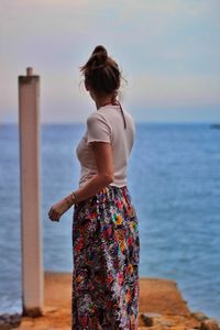 Rear view of woman standing at beach against sky