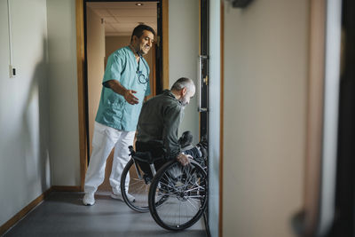 Happy doctor assisting patient in wheelchair at corridor of clinic