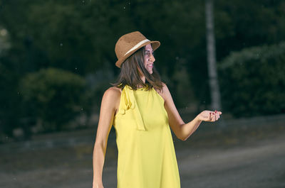 Woman wearing hat standing against trees on road