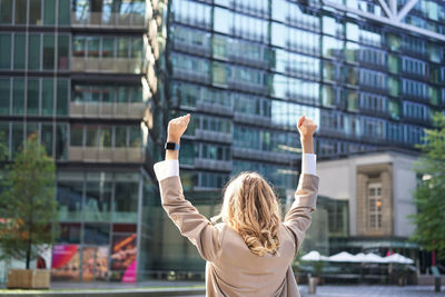 Rear view of woman with arms raised standing in city