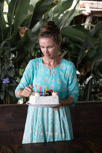 A caucasian girl is holding a cake on her birthday. wearing a green dress.