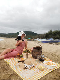 Rear view of woman sitting at beach against sky