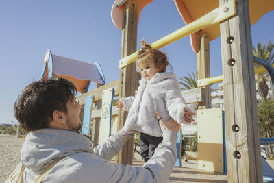 Father holding daughter standing on slide