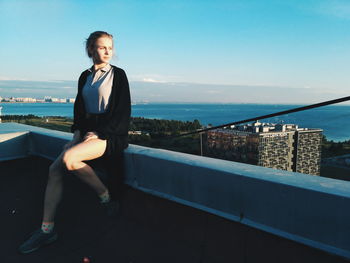 Young woman standing by railing against sea