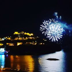Firework display over illuminated city against sky at night