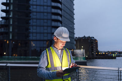 Engineer wearing hardhat using tablet pc by railing