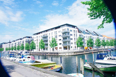 Boats moored on river by city against sky