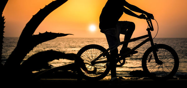 Silhouette of boy on a bicycle, sea and sunset in background. youth, vacation, holiday fun concept.