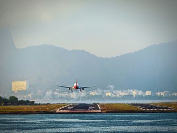 Airplane landing on runway by mountains against sky