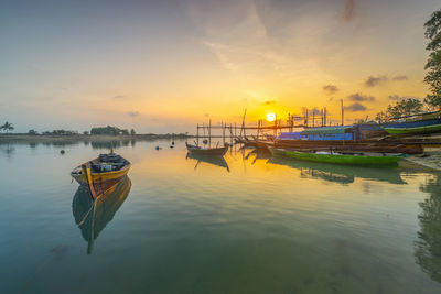 Boats moored in lake against sky during sunset