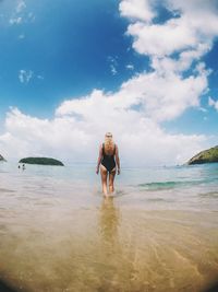 Rear view of seductive woman standing on shore at beach against sky