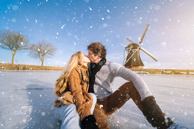 Couple kissing while sitting on snow covered landscape