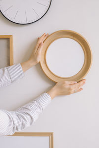 Cropped hand of woman holding picture frame against wall