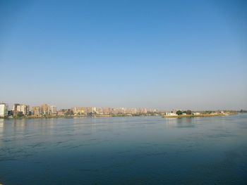 Sea by buildings against clear blue sky