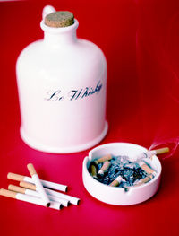 Close-up of whisky flask with cigarettes on red background