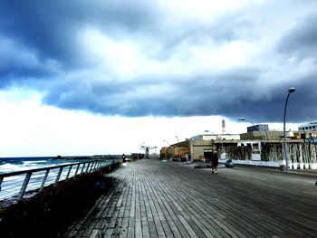 Empty road leading towards building against cloudy sky