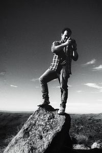 Young man standing on rock against sky
