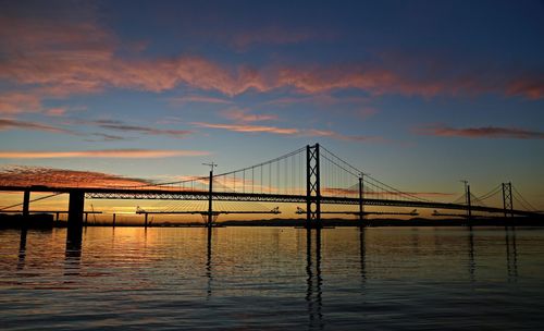 View of suspension bridge over calm sea at sunset