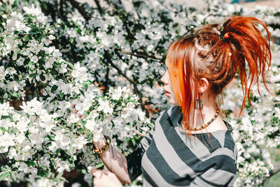 Side view of redhead young woman holding apple blossoms on tree
