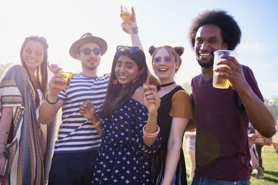 Friends holding drinks in glasses while dancing against sky