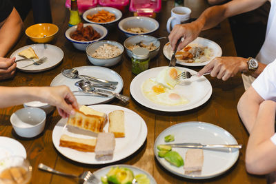 Man eating fried eggs breakfast with friends on wooden table.