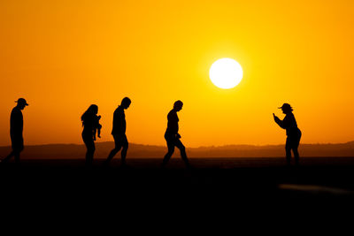 Group of people, in silhouette, are seen on the pier of porto da barra against the sunset 