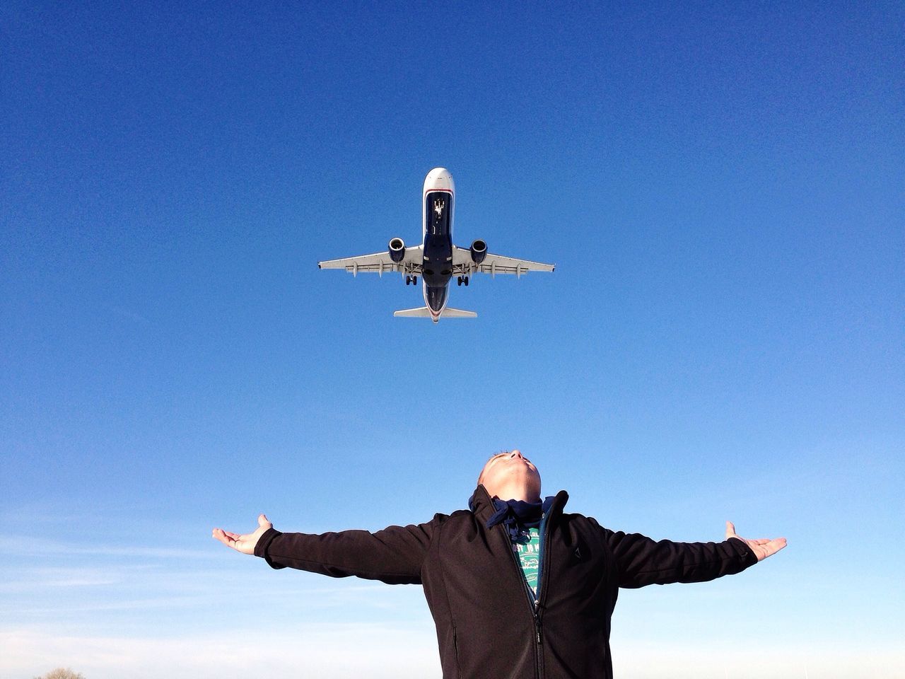 low angle view, clear sky, flying, airplane, blue, sky, mid-air, statue, copy space, air vehicle, sculpture, travel, leisure activity, human representation, lifestyles, art, art and craft, men