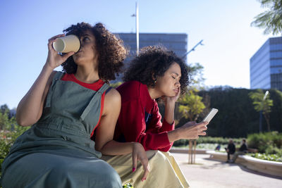 Young woman using smart phone while sitting on laptop