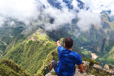 Rear view of sitting on rock while pointing at machu picchu