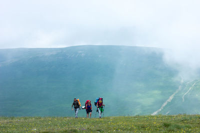 Hikers walking on field against mountain