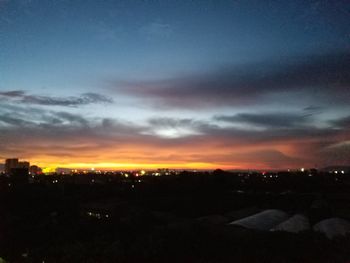 Silhouette city against dramatic sky during sunset