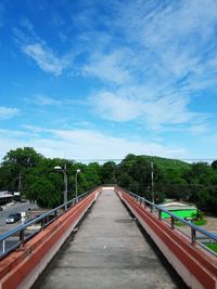 Walkway amidst trees against blue sky