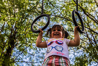 Low angle view of happy girl holding play equipment against trees