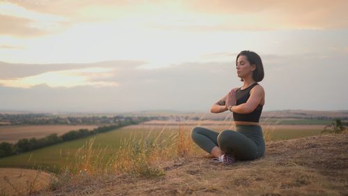 Young woman sitting on field against sky during sunset