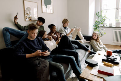 Teenage girls and boys using smart phones in living room at home