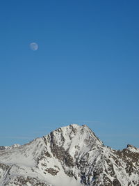 Low angle view of snow covered mountains against clear blue sky