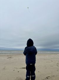 Rear view of man standing on beach against sky