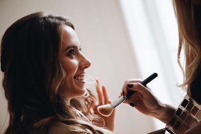 Beautician applying make-up on face of young woman 